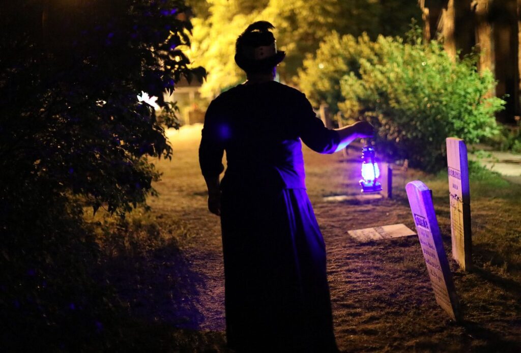 A figure on Halloween night carrying a purple lighted lantern casting a ghostly glow.